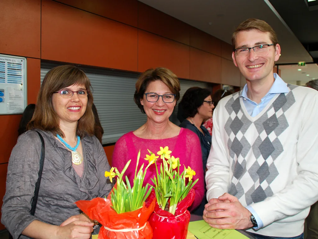 Drei Personen stehen mit Blumen im Foyer.